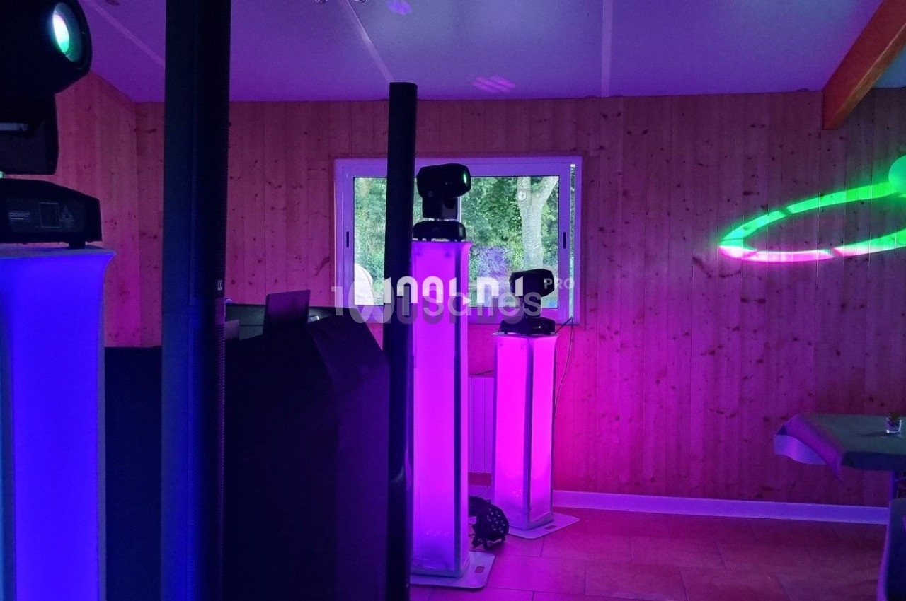 Équipements d'éclairage coloré dans une salle en bois, avec des tables dressées et des effets lumineux projetés.