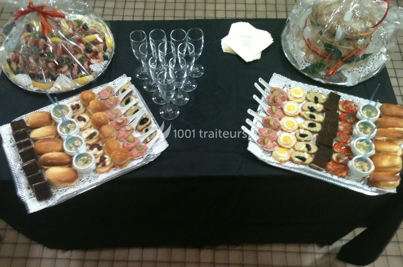 Table avec nappes noires présentant des plateaux de petits fours variés, verres à pied et paniers garnis emballés.