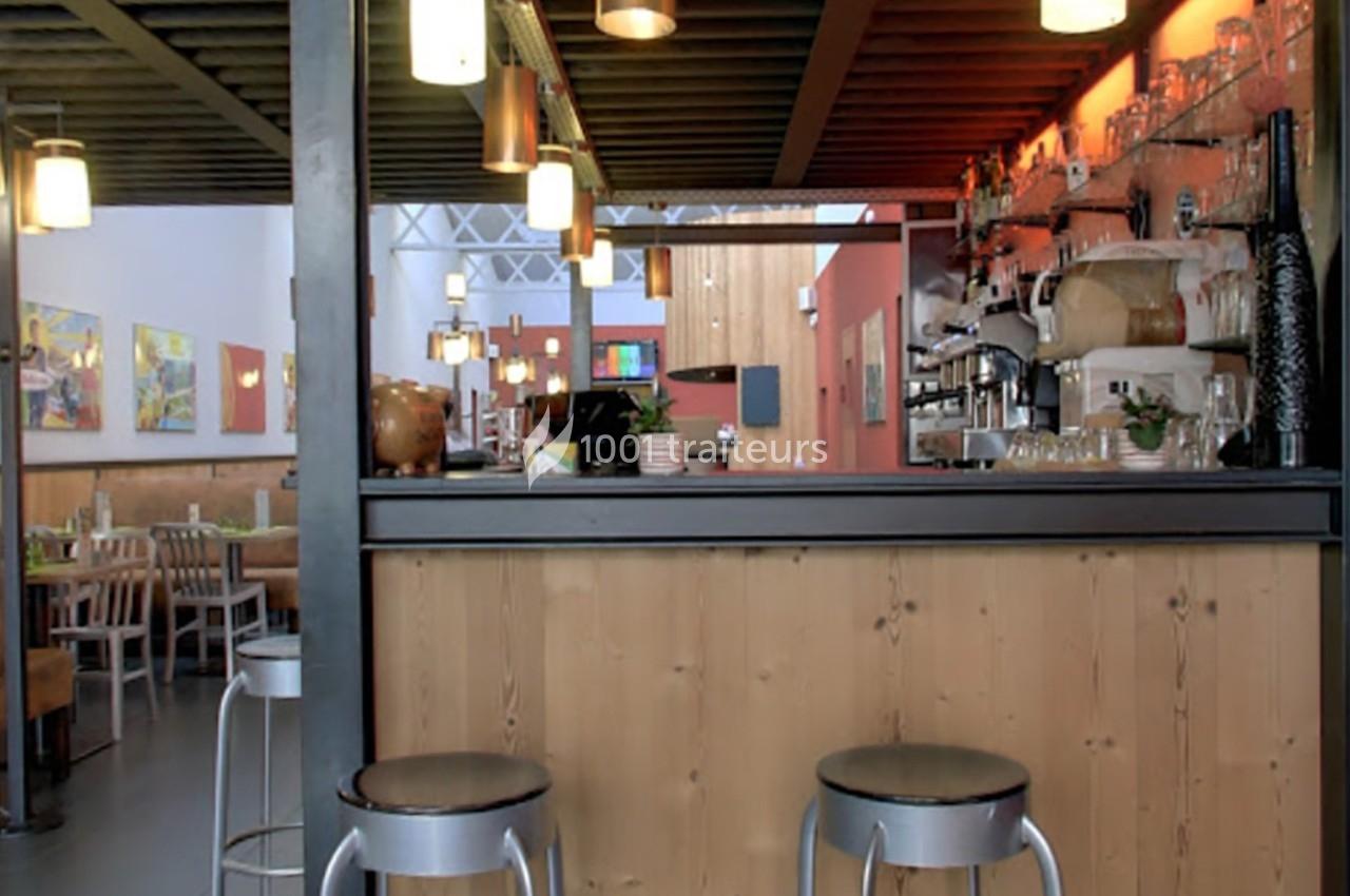 Intérieur d'un restaurant avec un bar en bois, des tabourets métalliques et des tables dressées en arrière-plan.