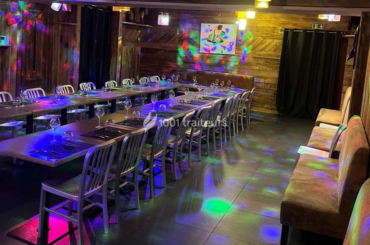 Salle de restaurant avec longues tables dressées, éclairage tamisé et effets lumineux colorés sur le sol.