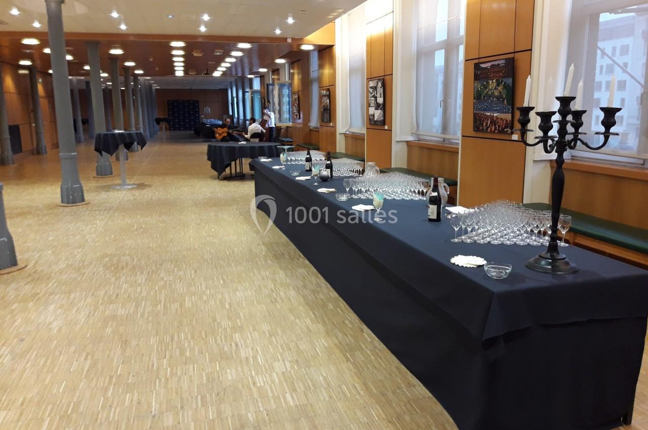Salle avec tables dressées pour un buffet, comprenant des verres, une bouteille et un chandelier noir.