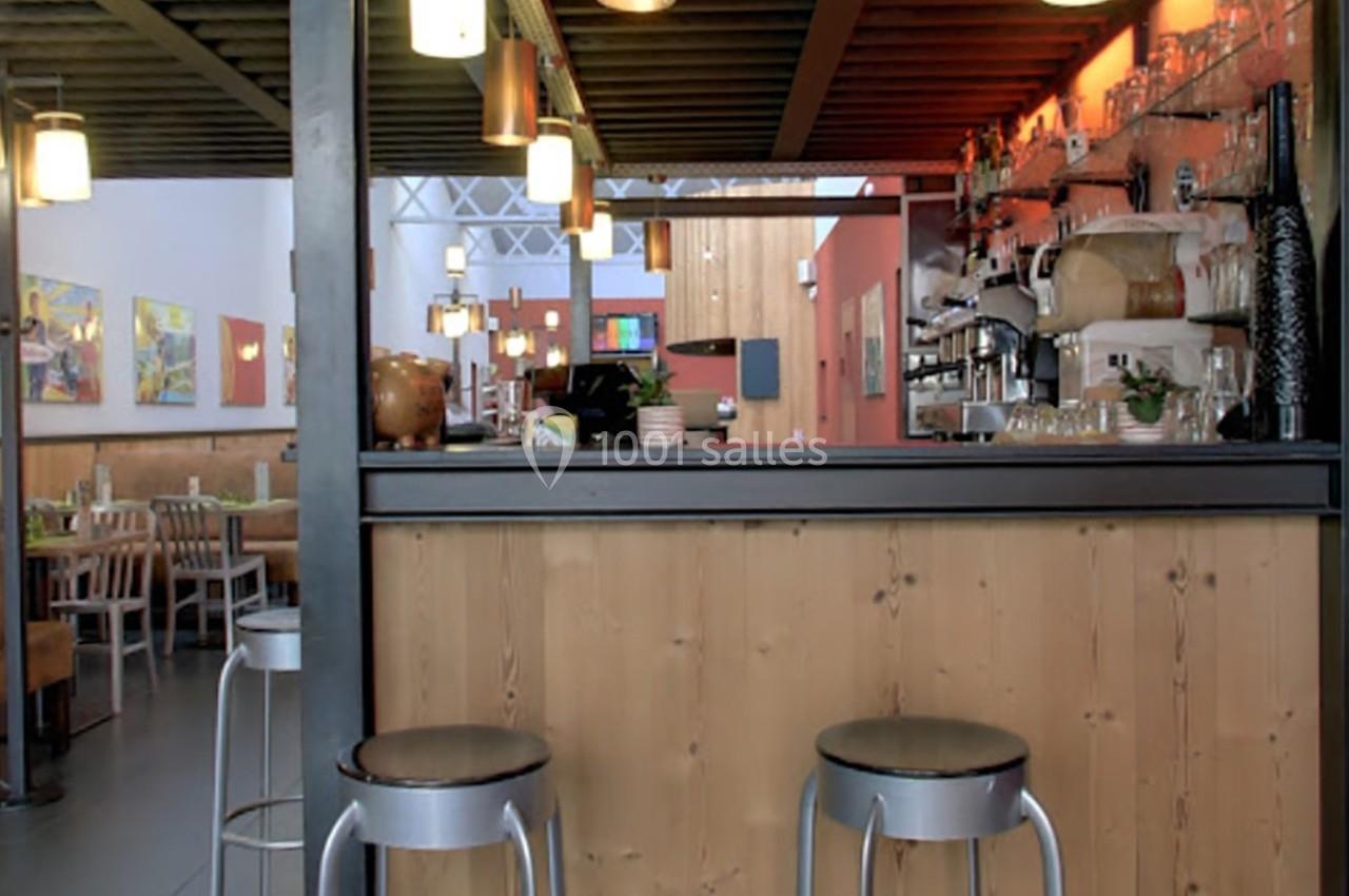 Comptoir de bar en bois avec tabourets métalliques, éclairage suspendu et tables en arrière-plan dans un restaurant.