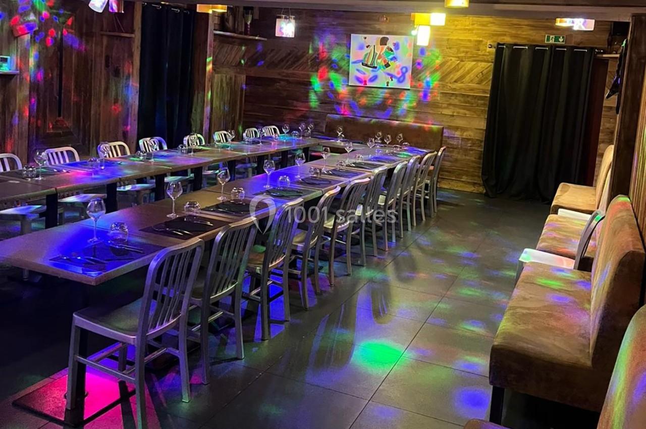 Salle de restaurant avec longues tables dressées, éclairage coloré et ambiance festive.