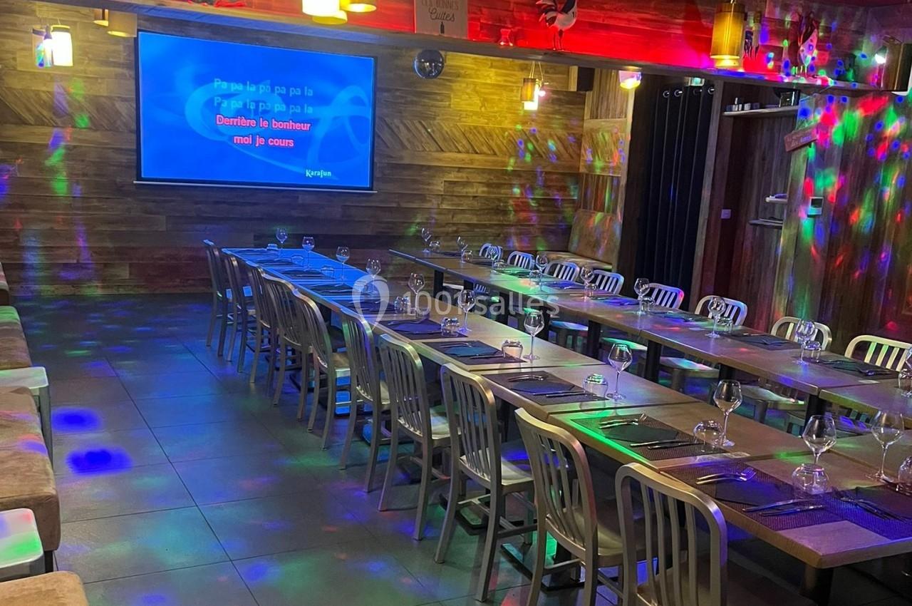 Salle de karaoké avec tables alignées, chaises métalliques et écran affichant des paroles de chanson.