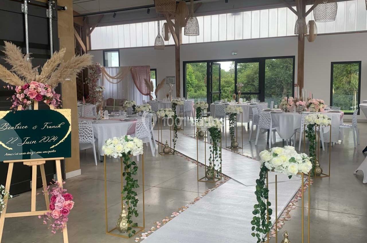 Salle de réception décorée pour un mariage avec allée centrale ornée de fleurs blanches et roses.