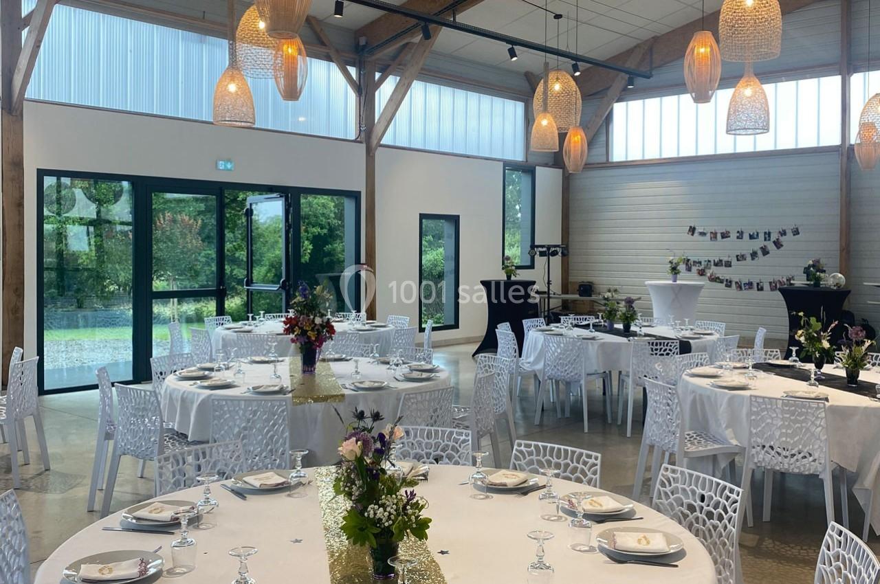 Salle de réception lumineuse avec tables dressées, décorations florales et suspensions en osier.