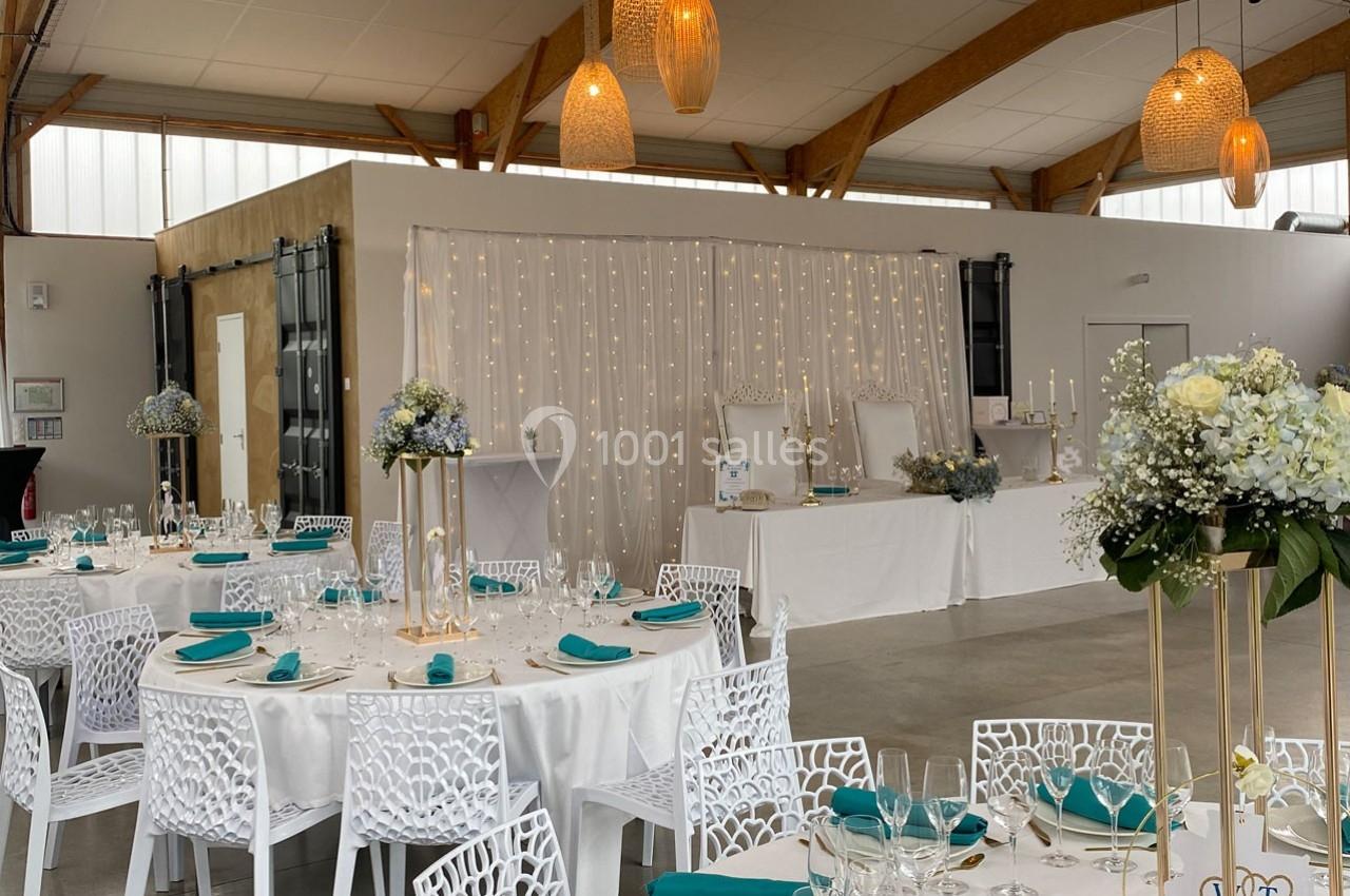 Salle de réception décorée avec des tables rondes, nappes blanches, chaises ajourées et éclairage chaleureux.