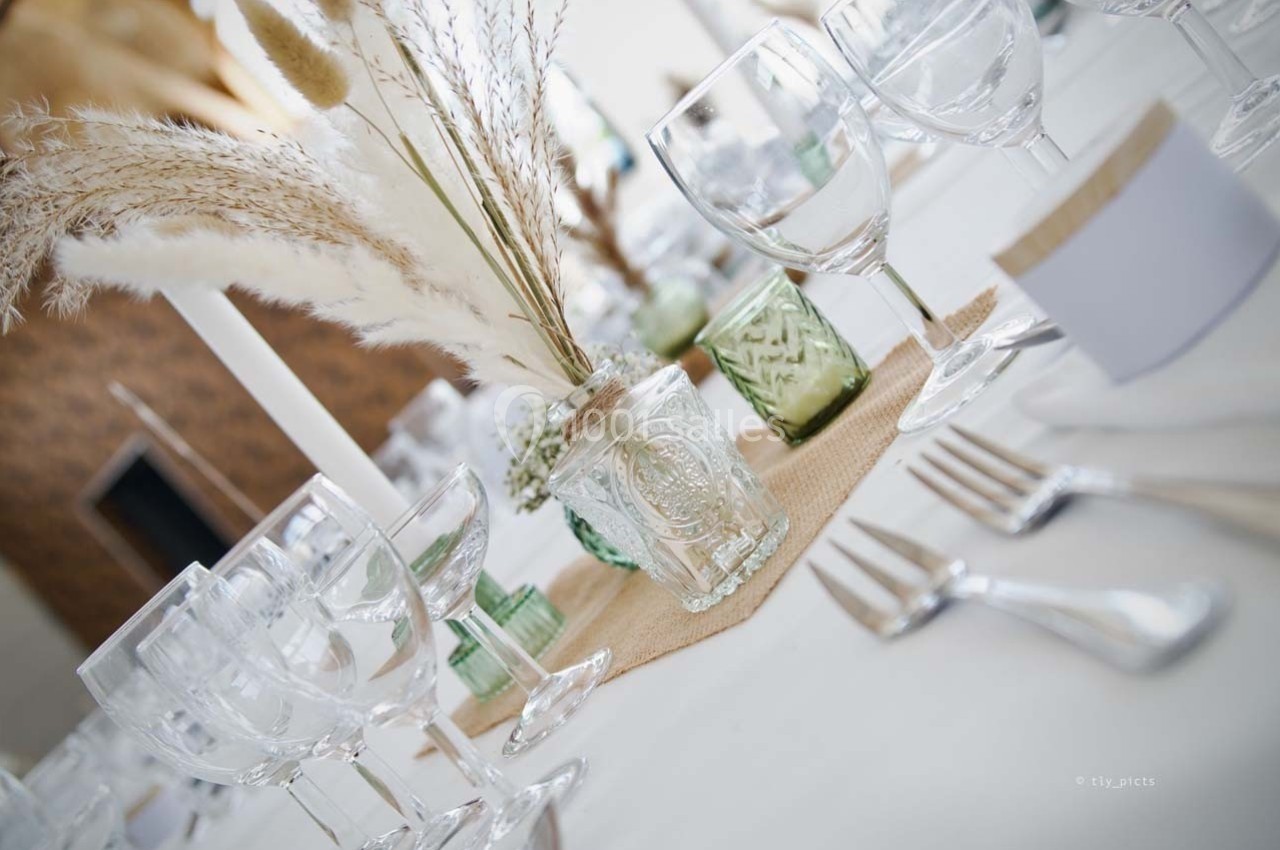 Table décorée avec des pampas, des verres en cristal et des bougies, sur une nappe blanche avec des détails en lin.