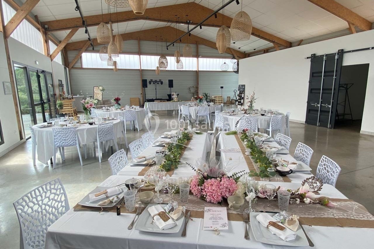 Salle de réception lumineuse décorée pour un événement, avec tables dressées et ornées de fleurs et de détails élégants.