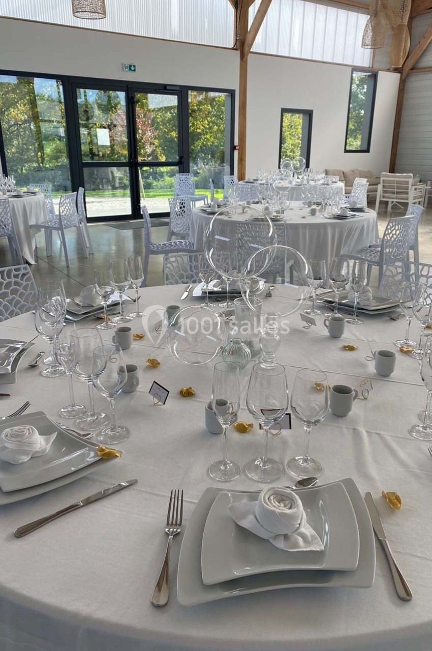 Table dressée pour un événement avec nappes blanches, vaisselle élégante, serviettes pliées et décoration sobre.