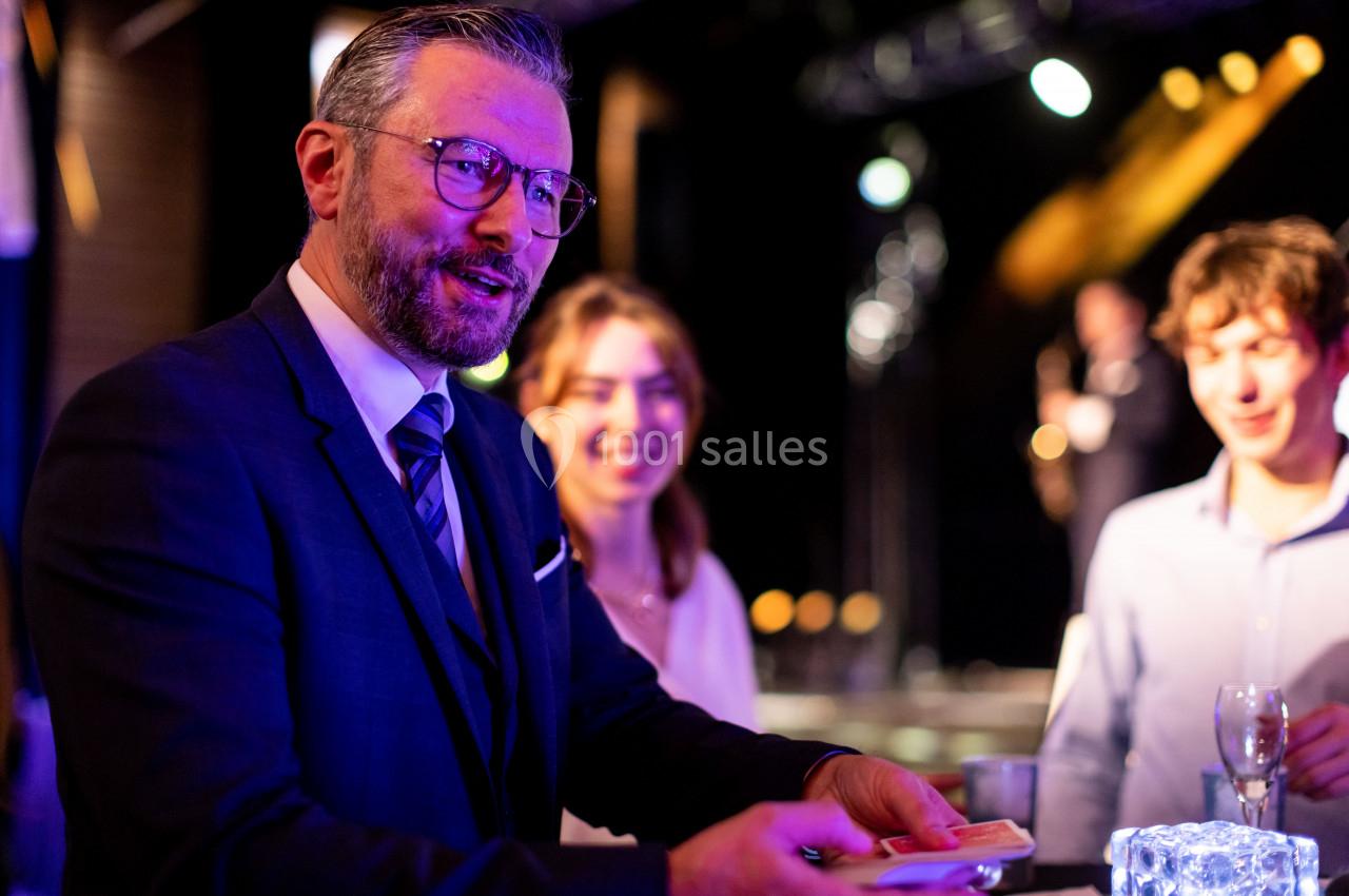 Un homme en costume effectue un tour de magie avec des cartes devant un petit groupe de personnes souriantes.