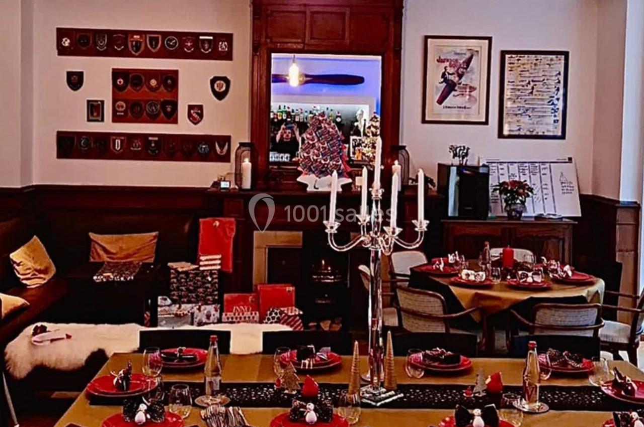 Salle de restaurant décorée avec des tables dressées, un chandelier central et des éléments de décoration murale.