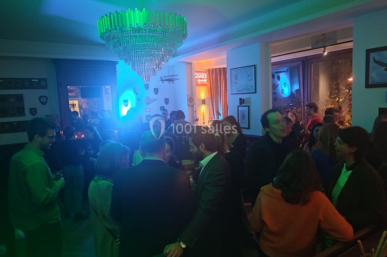 Groupe de personnes discutant dans une salle éclairée par des lumières colorées, ambiance festive en soirée.