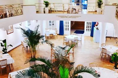 Intérieur d'un café lumineux avec canapés colorés, grandes fenêtres donnant sur une rue et un bar en arrière-plan.