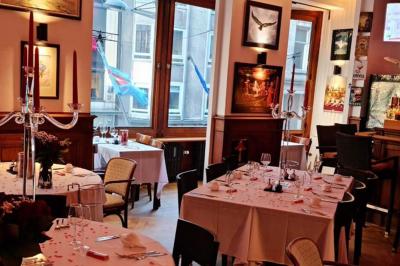 Intérieur d'un café lumineux avec canapés colorés, grandes fenêtres donnant sur une rue et un bar en arrière-plan.