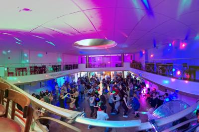 Intérieur d'un café lumineux avec canapés colorés, grandes fenêtres donnant sur une rue et un bar en arrière-plan.