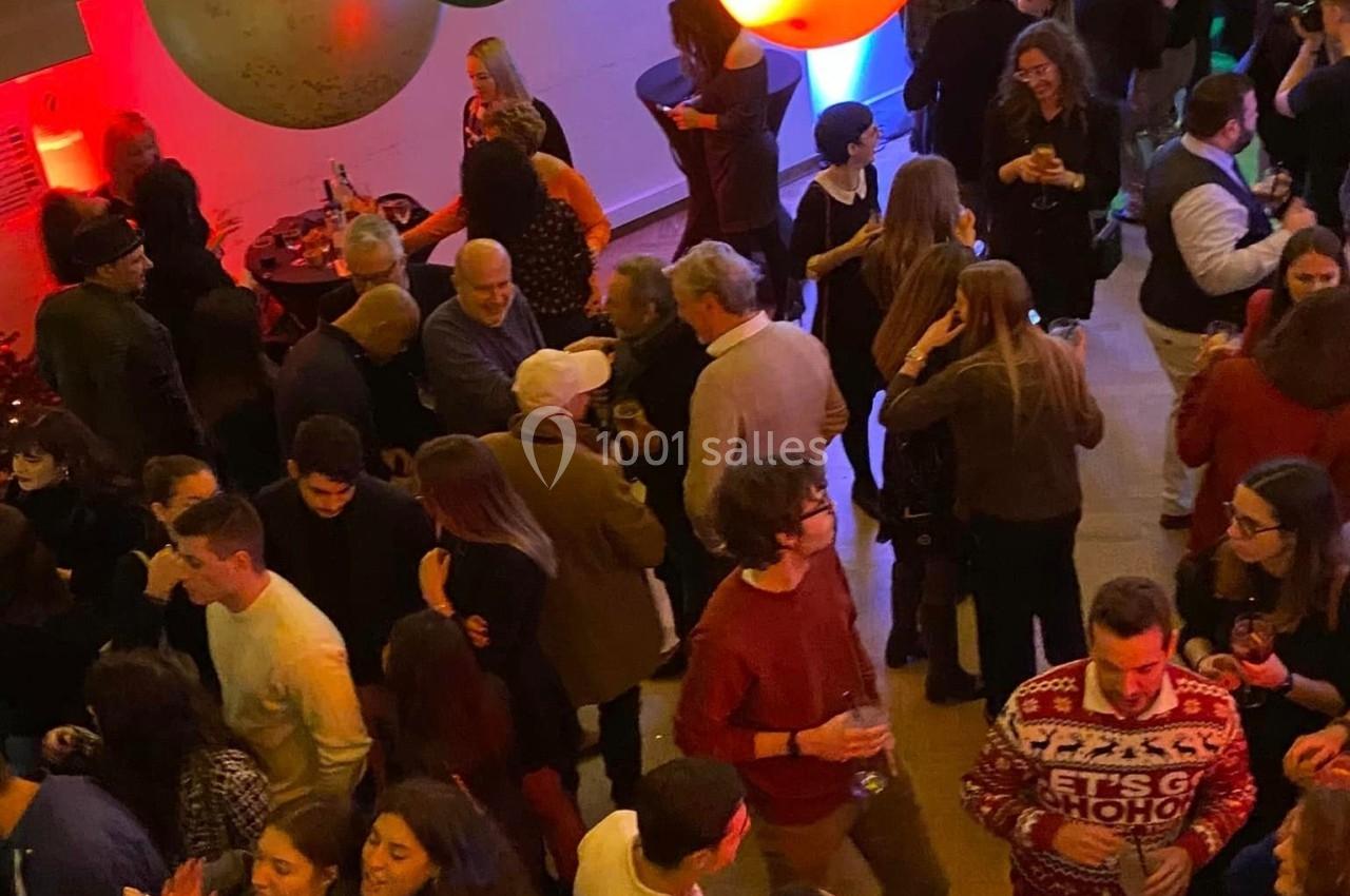Groupe de personnes dans une salle festive décorée de ballons colorés, discutant et dansant lors d'un événement.