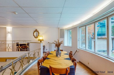 Intérieur d'un café lumineux avec canapés colorés, grandes fenêtres donnant sur une rue et un bar en arrière-plan.