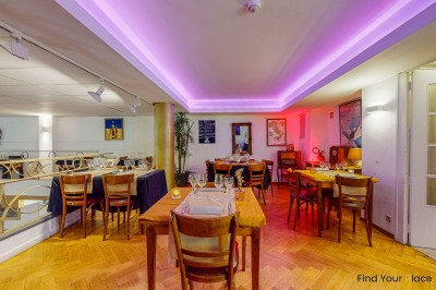 Intérieur d'un café lumineux avec canapés colorés, grandes fenêtres donnant sur une rue et un bar en arrière-plan.