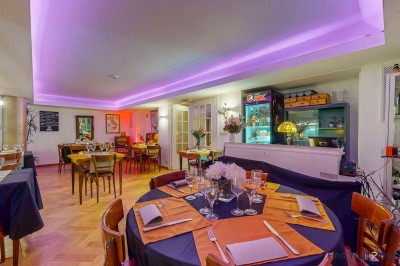 Intérieur d'un café lumineux avec canapés colorés, grandes fenêtres donnant sur une rue et un bar en arrière-plan.