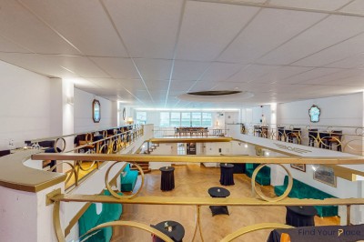 Intérieur d'un café lumineux avec canapés colorés, grandes fenêtres donnant sur une rue et un bar en arrière-plan.