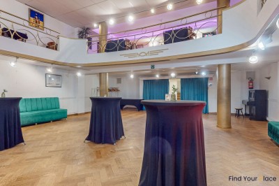 Intérieur d'un café lumineux avec canapés colorés, grandes fenêtres donnant sur une rue et un bar en arrière-plan.