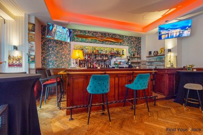 Intérieur d'un café lumineux avec canapés colorés, grandes fenêtres donnant sur une rue et un bar en arrière-plan.