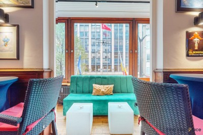 Intérieur d'un café lumineux avec canapés colorés, grandes fenêtres donnant sur une rue et un bar en arrière-plan.