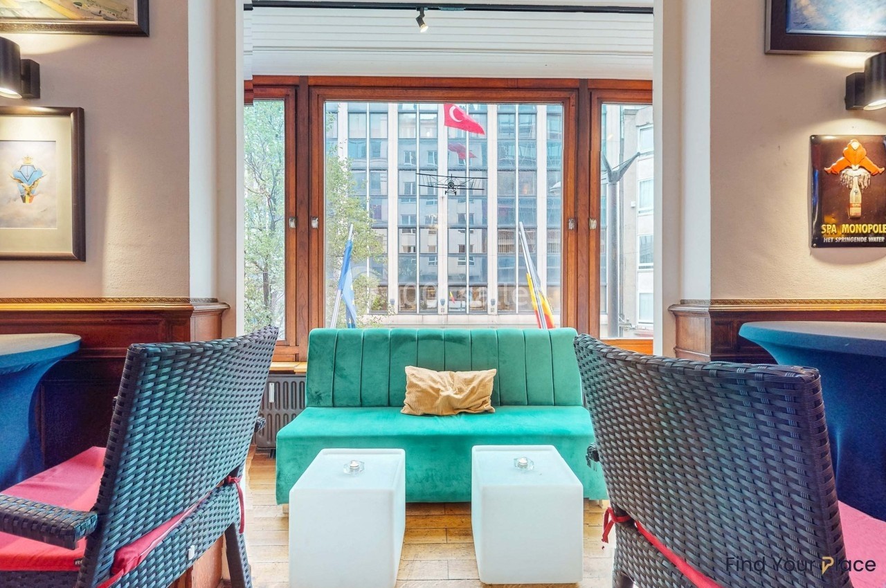 Canapé vert et tables basses blanches dans un salon avec vue sur des drapeaux et des bâtiments à travers une grande fenêtre.