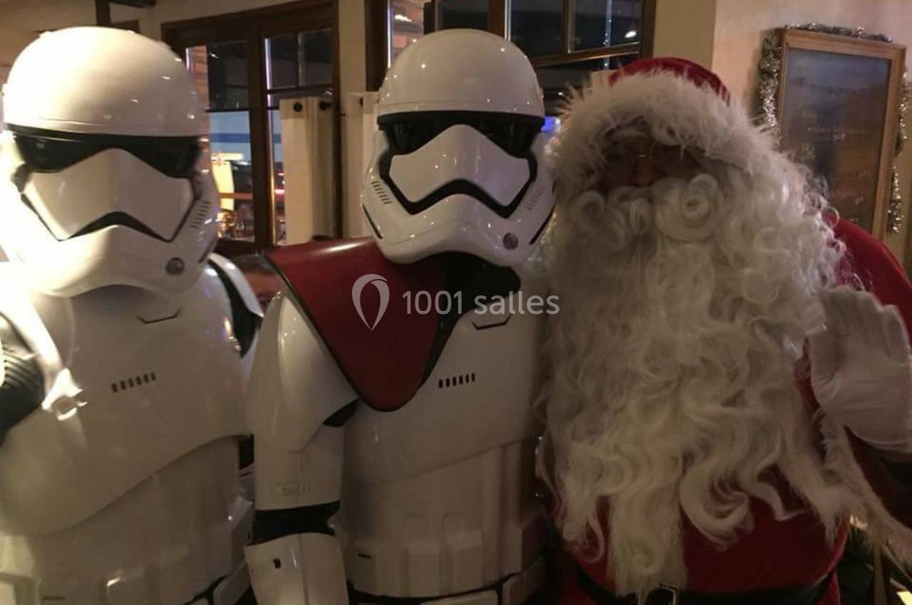 Deux personnes en costumes de Stormtroopers posent avec un homme déguisé en Père Noël dans un intérieur faiblement éclairé.