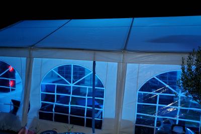 Grande tente blanche rectangulaire installée sur un parking, entourée de végétation et de barrières de sécurité.