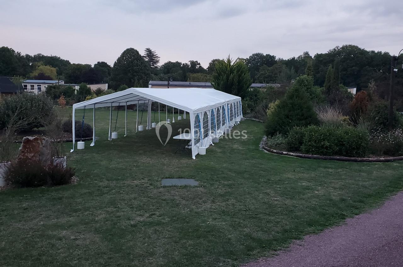 Tente blanche installée sur une pelouse dans un jardin, entourée de végétation et d'un chemin en gravier.