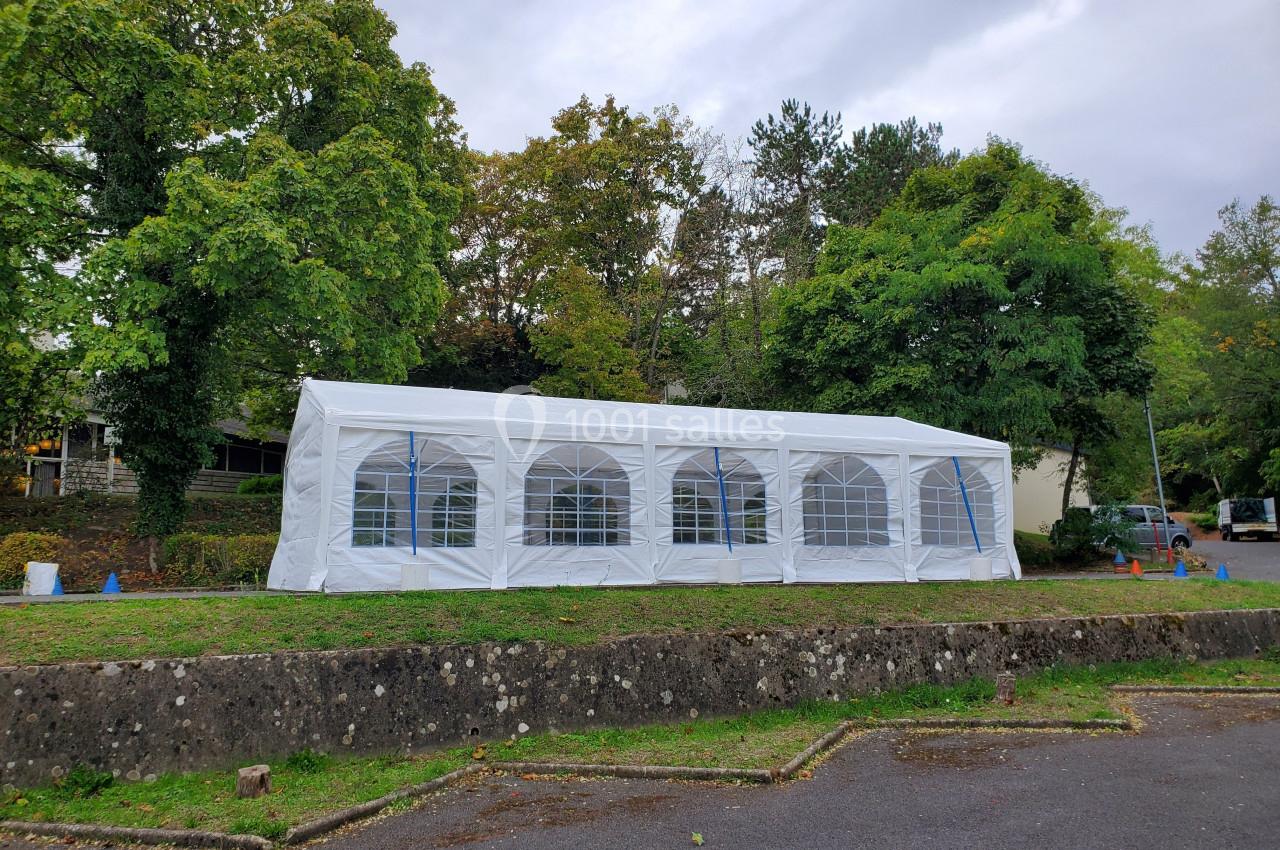 Grande tente blanche avec fenêtres transparentes installée sur une pelouse, entourée d'arbres et d'un parking.