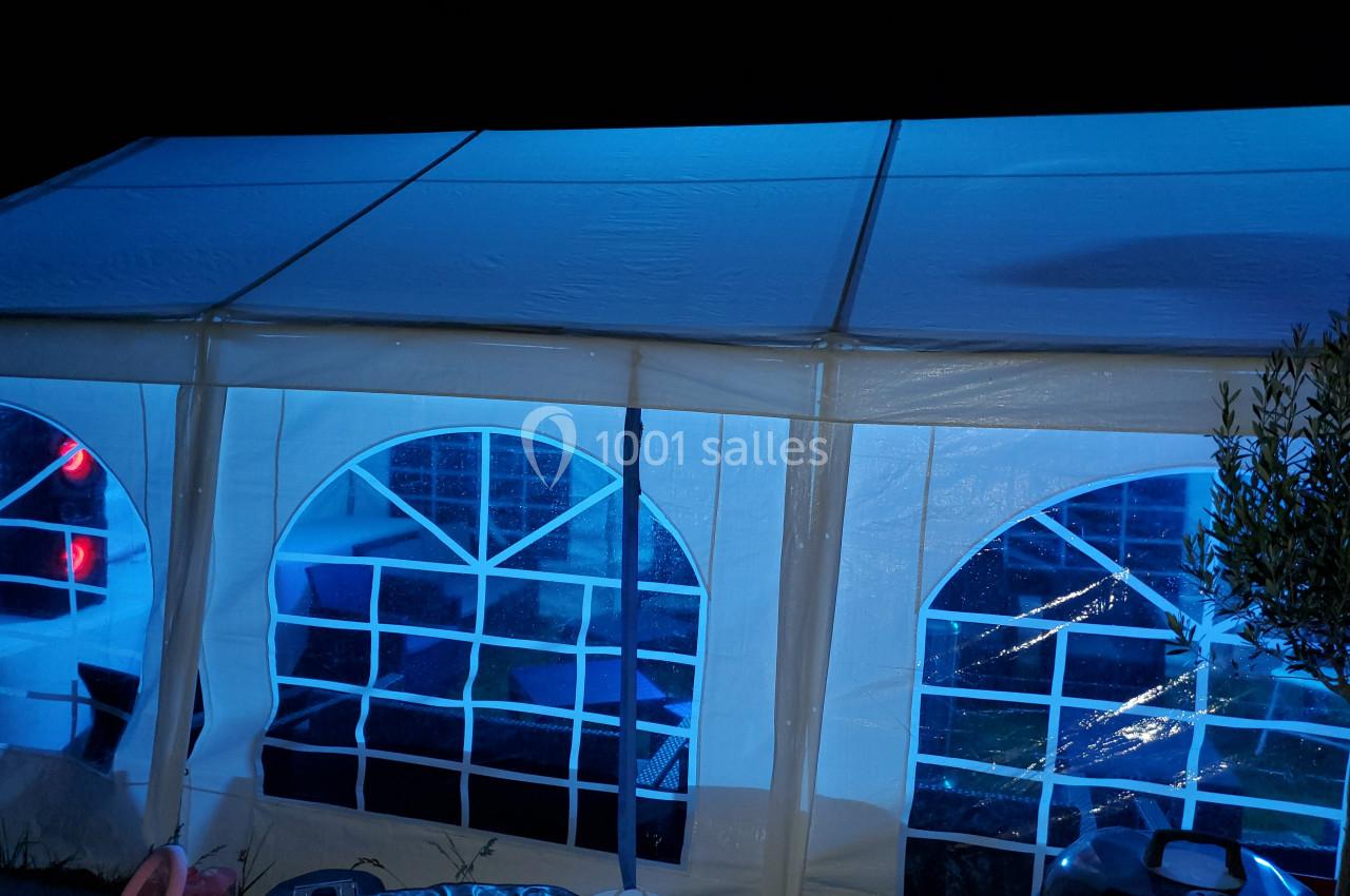 Tente blanche éclairée en bleu de nuit, avec fenêtres en arc de cercle laissant entrevoir un intérieur faiblement visible.