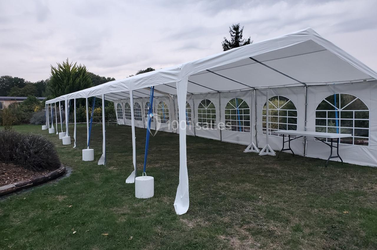 Grande tente blanche avec fenêtres en plastique transparent, installée sur une pelouse sous un ciel nuageux.