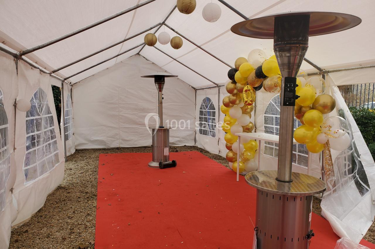 Intérieur d'une tente blanche avec tapis rouge, décorations de ballons jaunes et blancs, et deux chauffages d'extérieur.