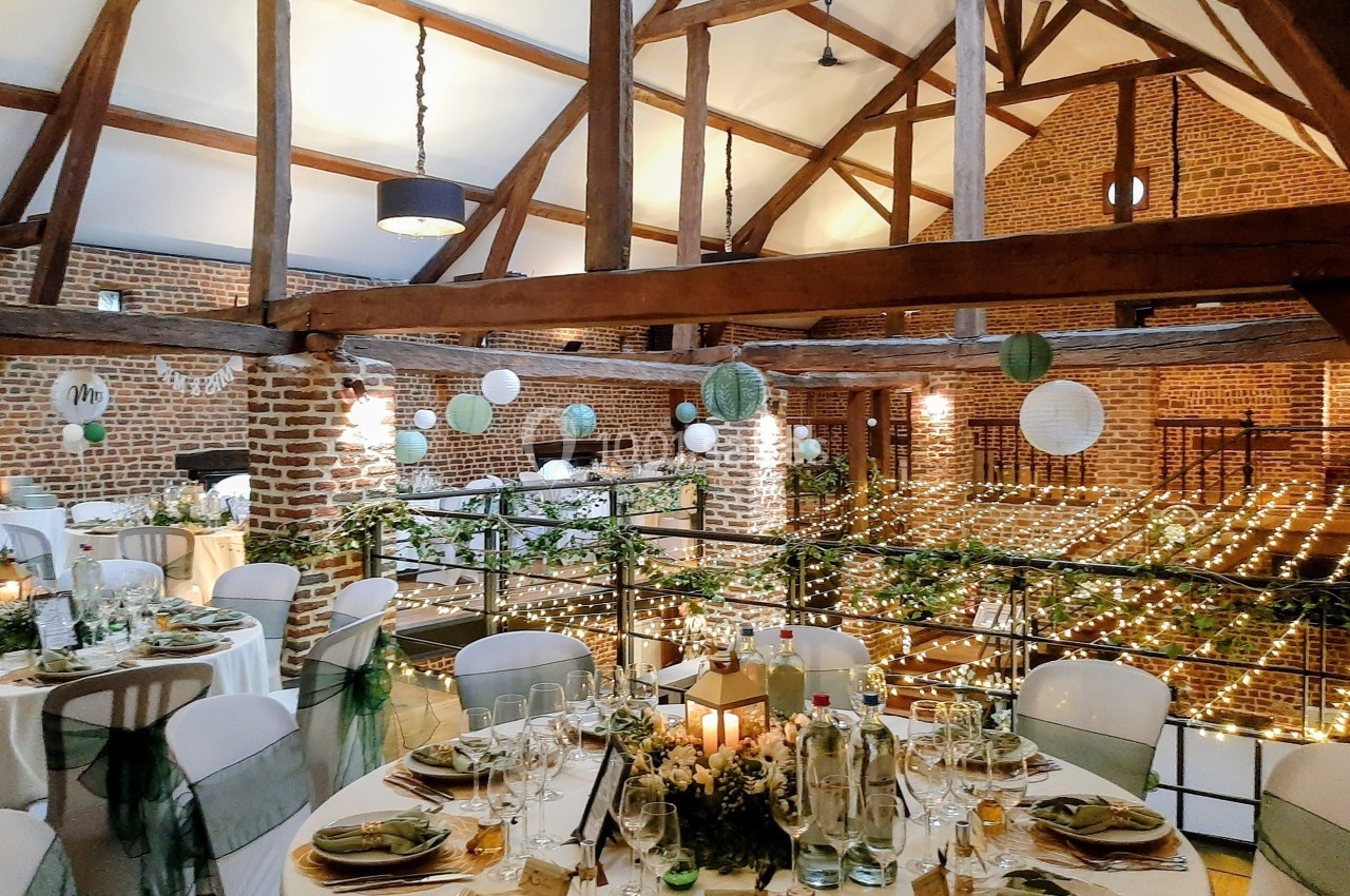 Salle de réception décorée avec des guirlandes lumineuses, des tables dressées et des suspensions en papier.