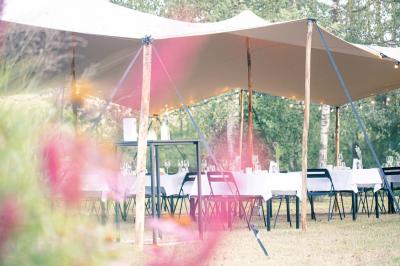 Jardin verdoyant avec arbres, pelouse soignée, tables hautes sous parasols et mobilier coloré près d'un plan d'eau.