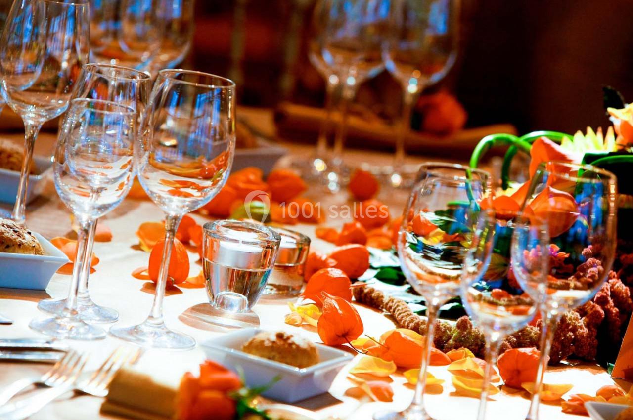 Table décorée avec des verres à pied, pétales orange, bougies et plats, dans une ambiance chaleureuse.