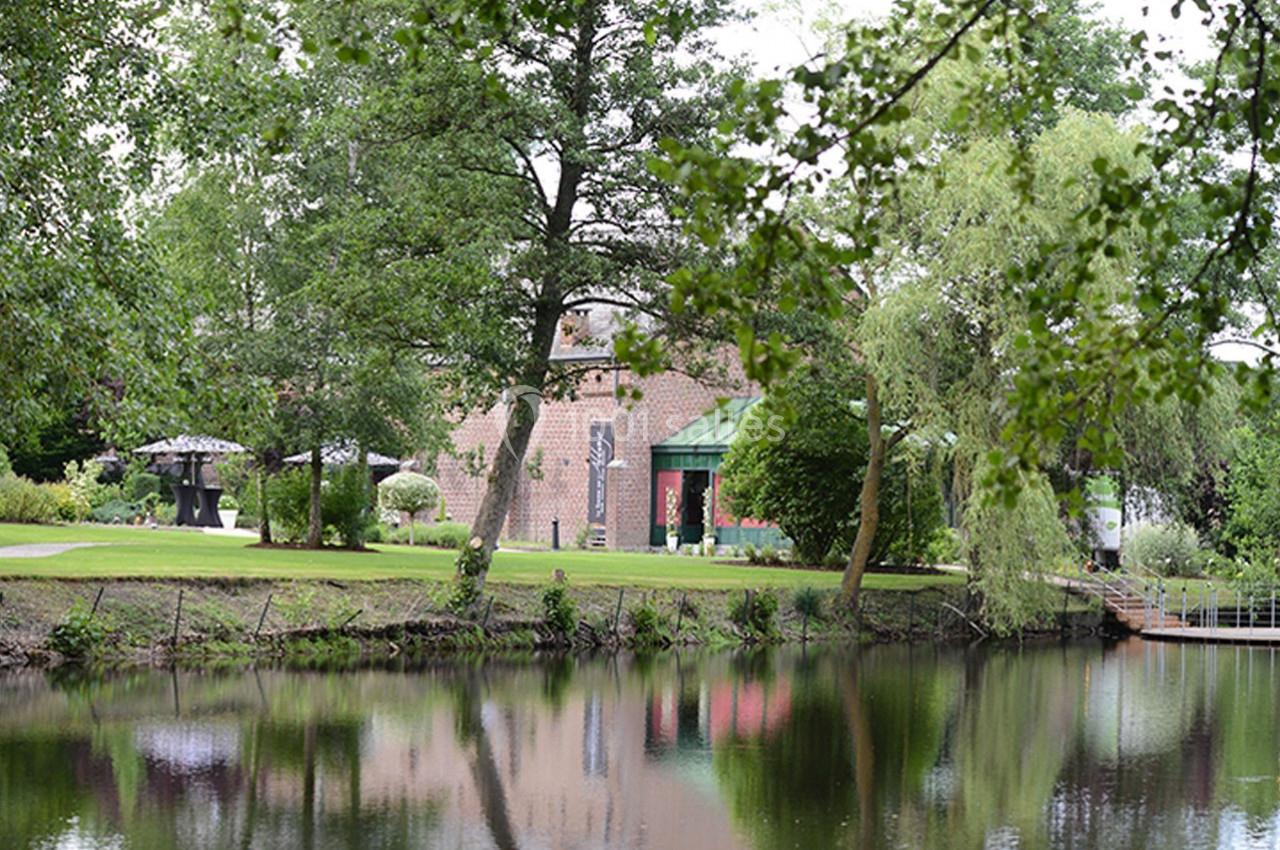 Vue d'un bâtiment en briques entouré d'arbres et d'un jardin, avec un étang au premier plan.
