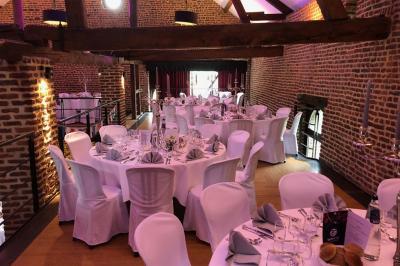 Jardin verdoyant avec arbres, pelouse soignée, tables hautes sous parasols et mobilier coloré près d'un plan d'eau.
