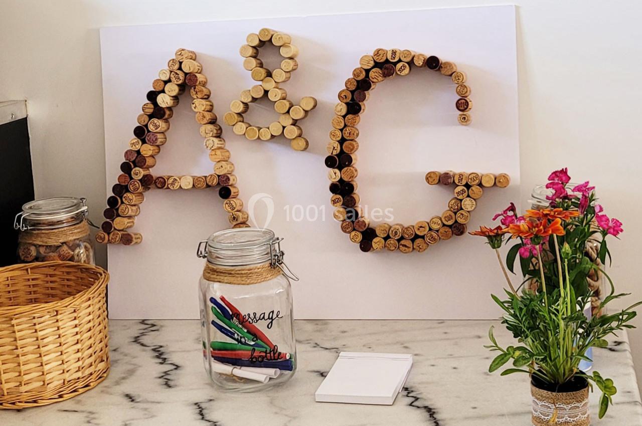 Location salle Bailleau-l'Évêque (Eure-et-Loir) - Le Domaine du Moulin 28 & SPA #24 Lettres ’A & G’ formées avec des bouchons en liège, entourées de pots en verre, d'un panier et d'un vase de fleurs.
