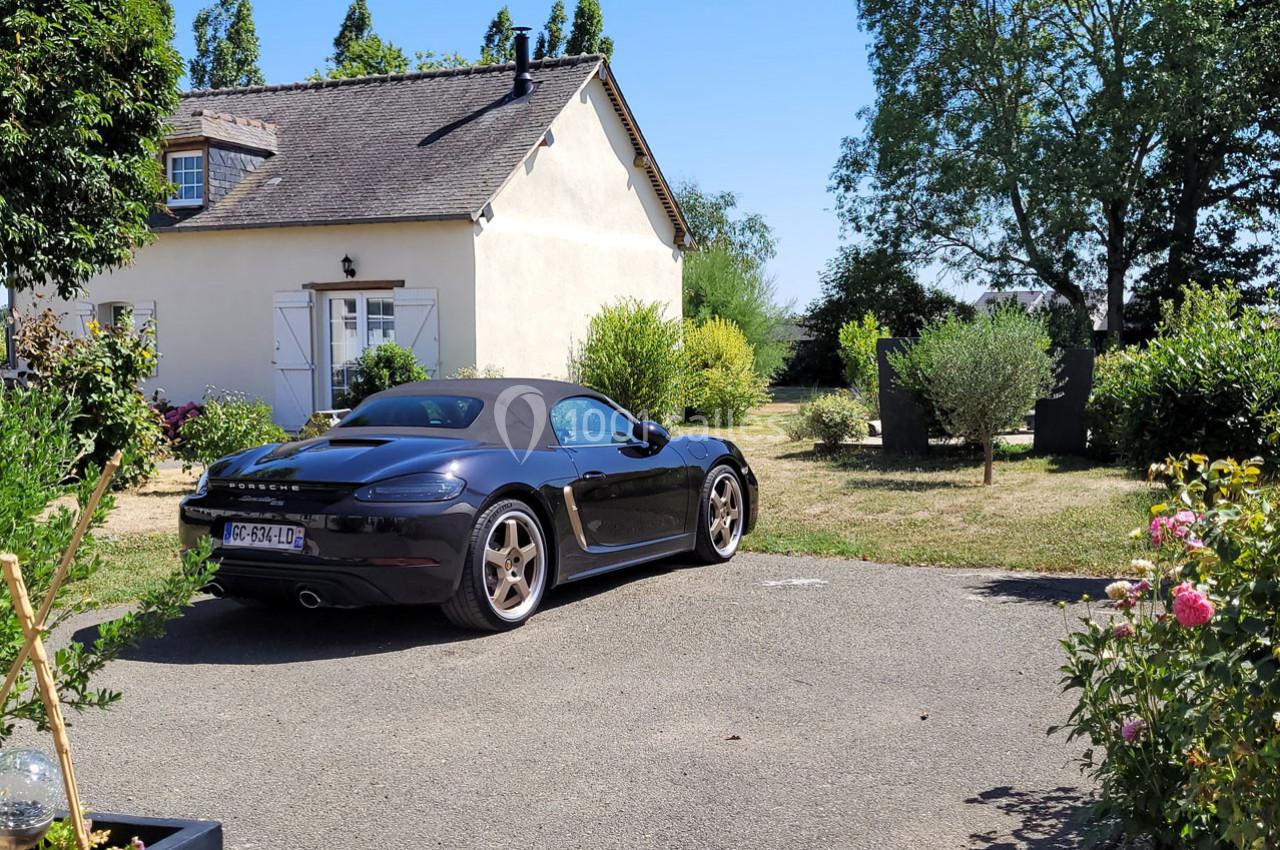 Location salle Bailleau-l'Évêque (Eure-et-Loir) - Le Domaine du Moulin 28 & SPA #34 Voiture décapotable noire garée dans une allée devant une maison avec jardin arboré en arrière-plan.