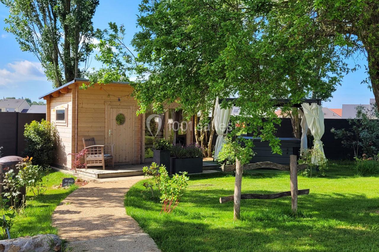 Location salle Bailleau-l'Évêque (Eure-et-Loir) - Le Domaine du Moulin 28 & SPA #5 Abri en bois et pergola avec rideaux blancs dans un jardin verdoyant, chemin en pierre menant à l'entrée.