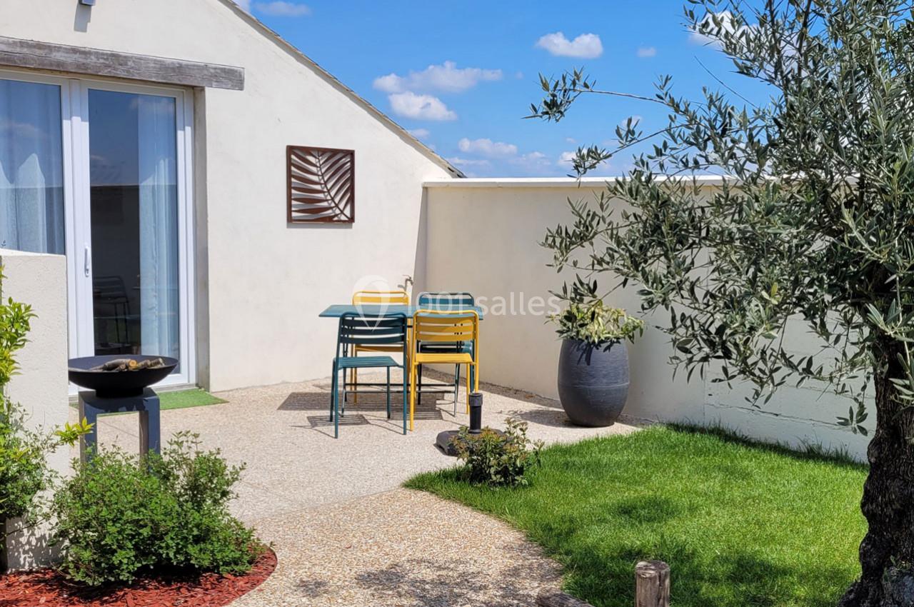 Location salle Bailleau-l'Évêque (Eure-et-Loir) - Le Domaine du Moulin 28 & SPA #6 Terrasse extérieure avec table et chaises colorées, barbecue, olivier en pot et pelouse sous un ciel bleu.