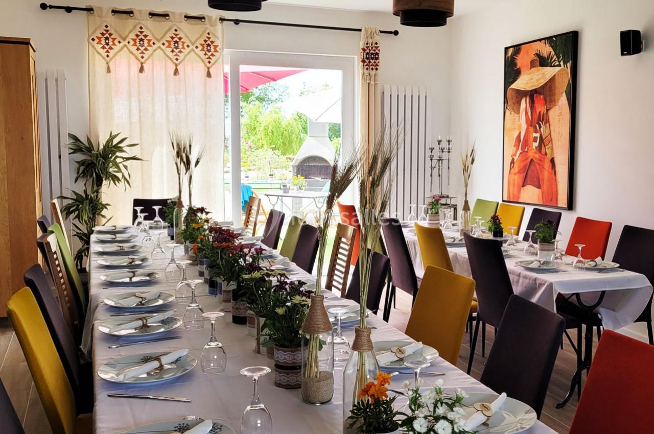 Location salle Bailleau-l'Évêque (Eure-et-Loir) - Le Domaine du Moulin 28 & SPA #14 Salle lumineuse avec deux longues tables dressées, décorées de fleurs et entourées de chaises colorées.