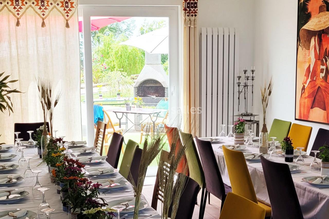 Location salle Bailleau-l'Évêque (Eure-et-Loir) - Le Domaine du Moulin 28 & SPA #15 Salle lumineuse avec tables dressées pour un repas, vue sur un jardin avec barbecue à travers une baie vitrée.