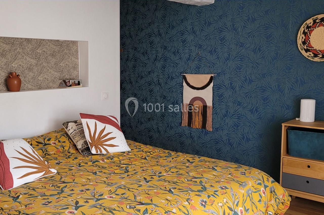 Location salle Bailleau-l'Évêque (Eure-et-Loir) - Le Domaine du Moulin 28 & SPA #28 Chambre avec un lit à motif floral, mur bleu texturé, étagère intégrée et décoration murale en tissu et osier.