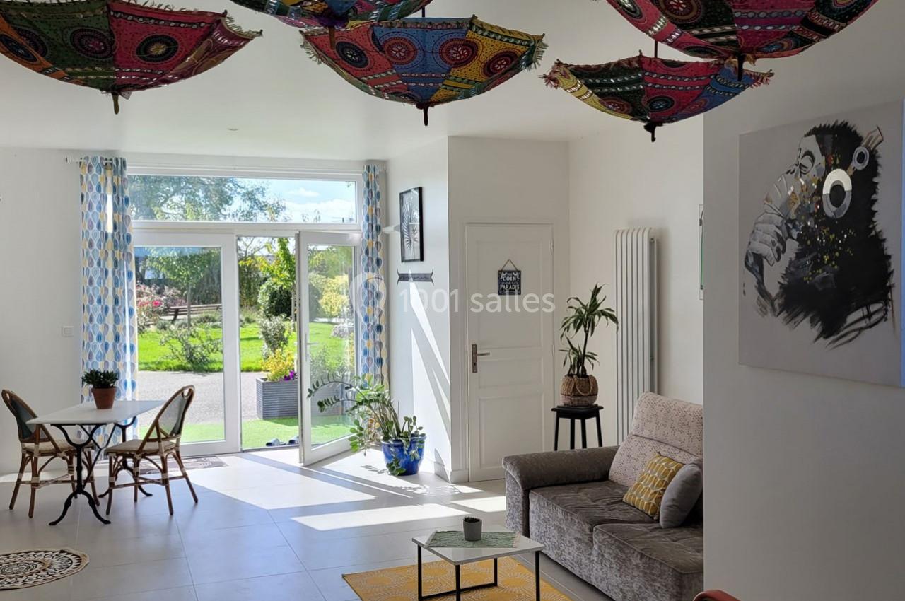 Location salle Bailleau-l'Évêque (Eure-et-Loir) - Le Domaine du Moulin 28 & SPA #20 Salon lumineux avec canapés, table ronde, plantes, grandes baies vitrées et parasols colorés suspendus au plafond.