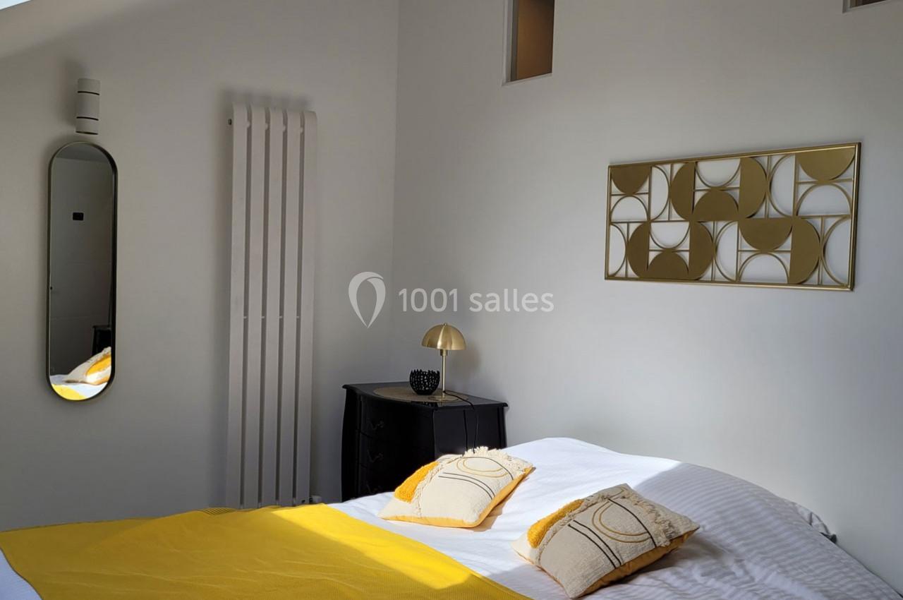 Location salle Bailleau-l'Évêque (Eure-et-Loir) - Le Domaine du Moulin 28 & SPA #33 Chambre lumineuse avec lit double, couvre-lit jaune, coussins assortis, miroir, radiateur et décoration murale dorée.